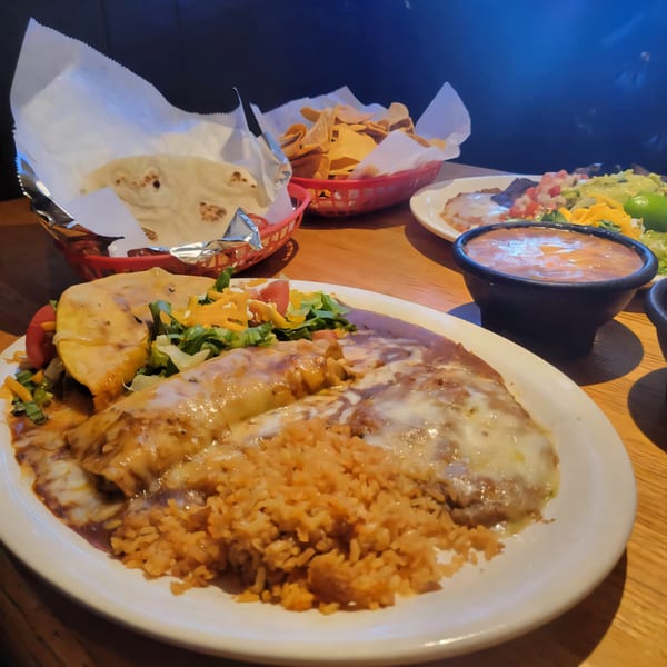 Kico's Mexican Food enchiladas with rice, beans, salad, tortillas, and chips on a wooden table.