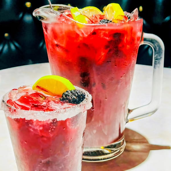 A pitcher and glass of Kico's red Mexican drink, garnished with lemon and blackberries.
