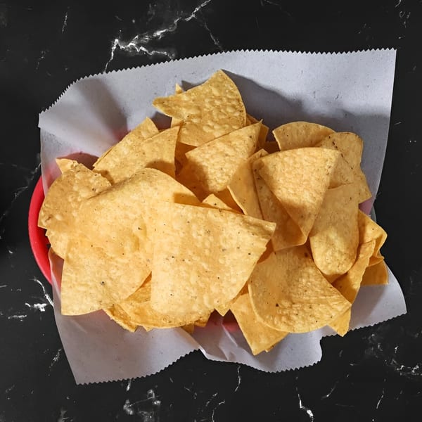 A red basket filled with Kico's Méxican Food tortilla chips on a dark marble surface.