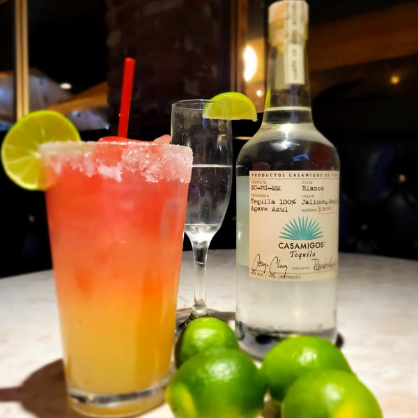 A vibrant Kico's Mexican Food margarita, tequila bottle, and limes on a table.